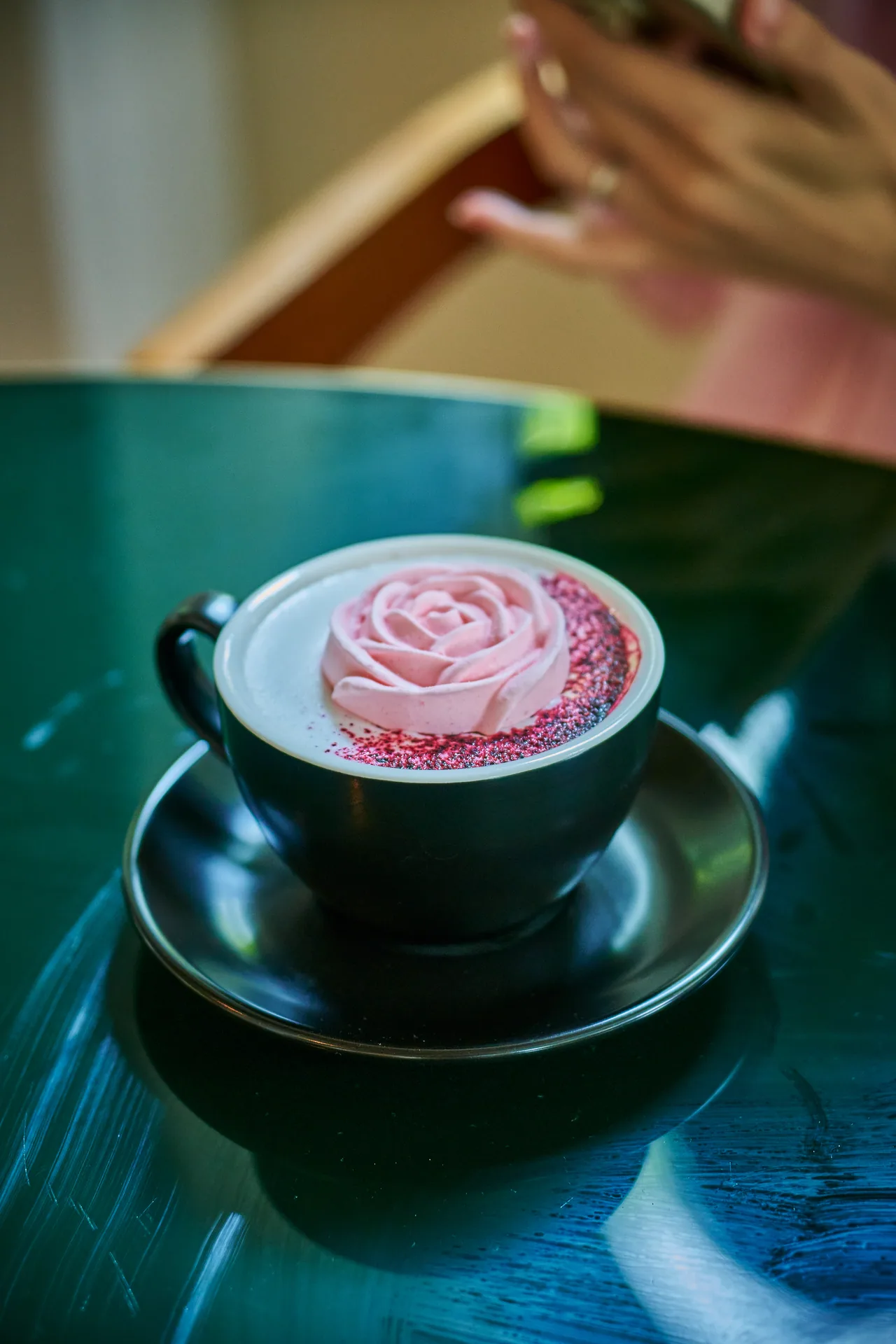 Rose latte art in a dark cup on a green marble café table