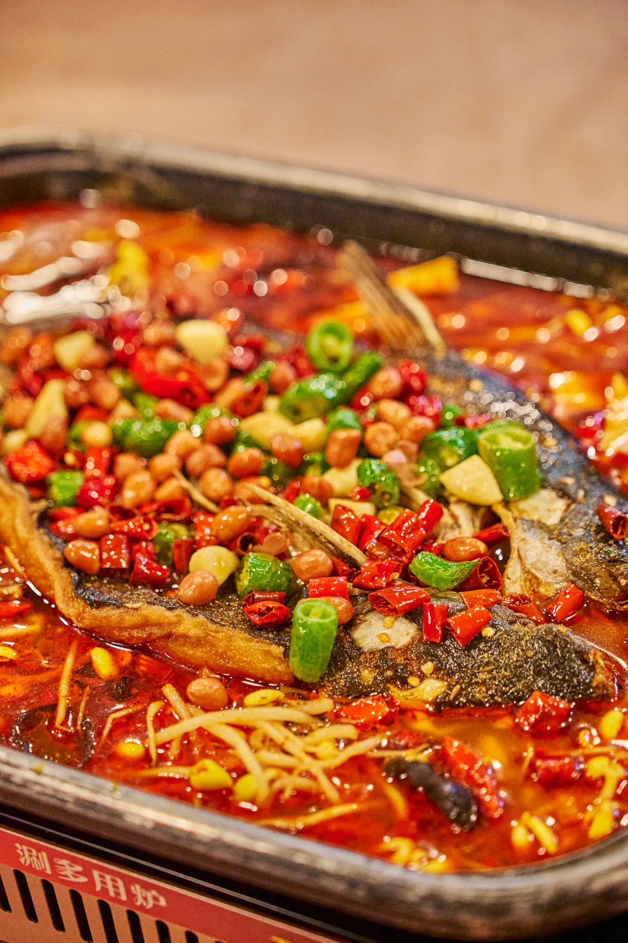Grilled whole fish in a tray of chilli oil with peanuts, green chillies and peppers