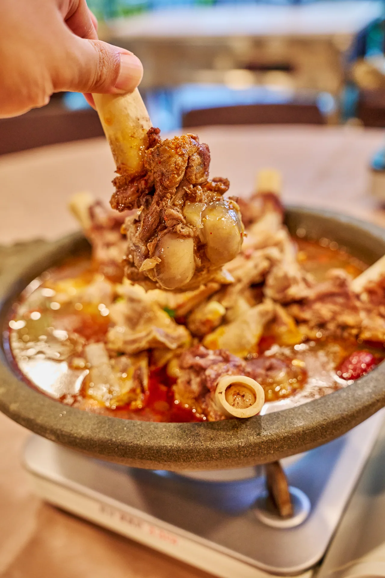 Hand lifting a lamb bone from a claypot of spicy lamb stew