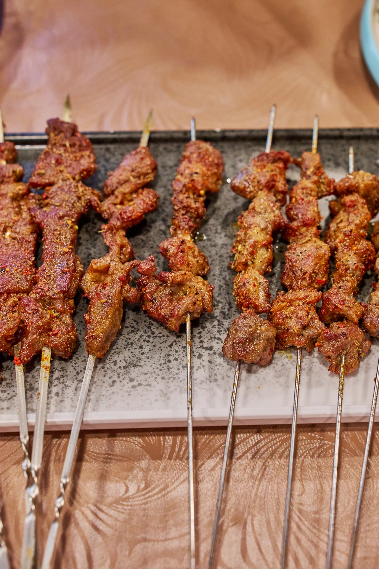 Row of spiced lamb skewers on a stone tray