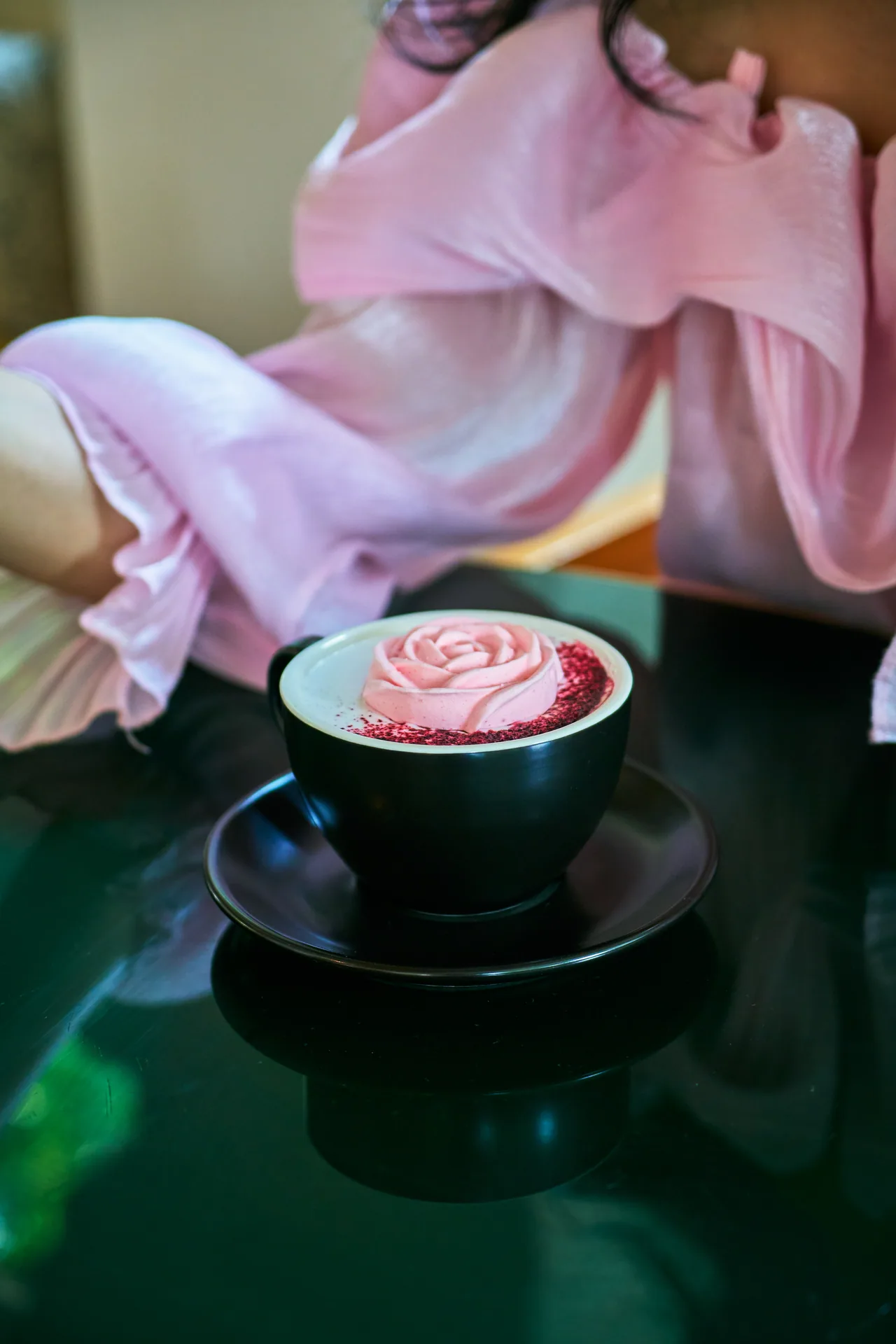 Latte with pink rose latte art on a dark green table