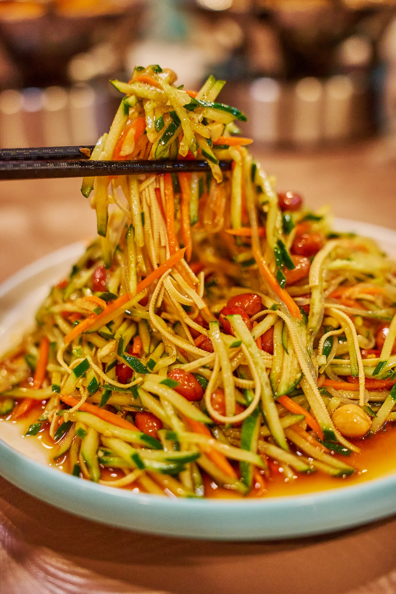 Chopsticks lifting shredded cucumber and carrot salad from the plate