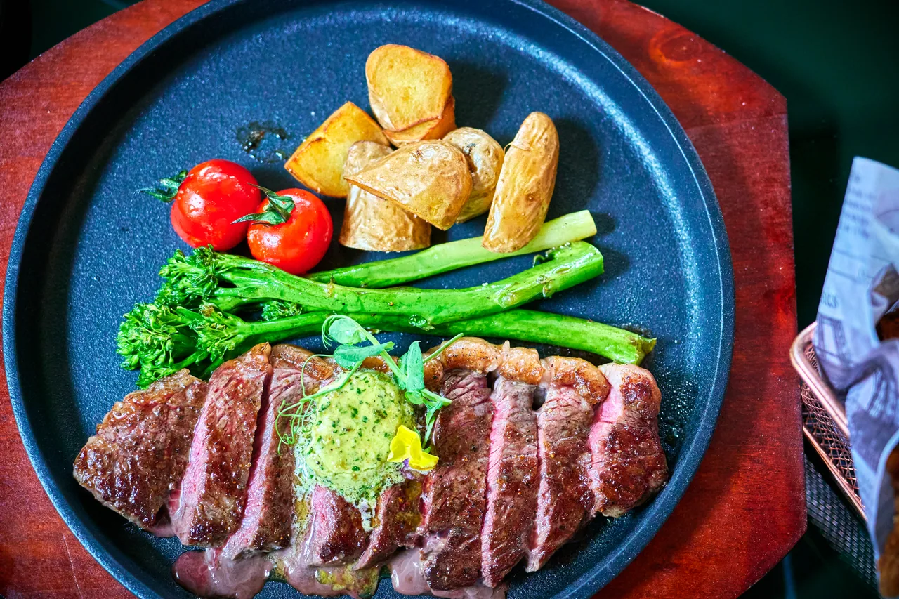 Sliced steak with broccolini, cherry tomatoes and roast potatoes on a dark plate