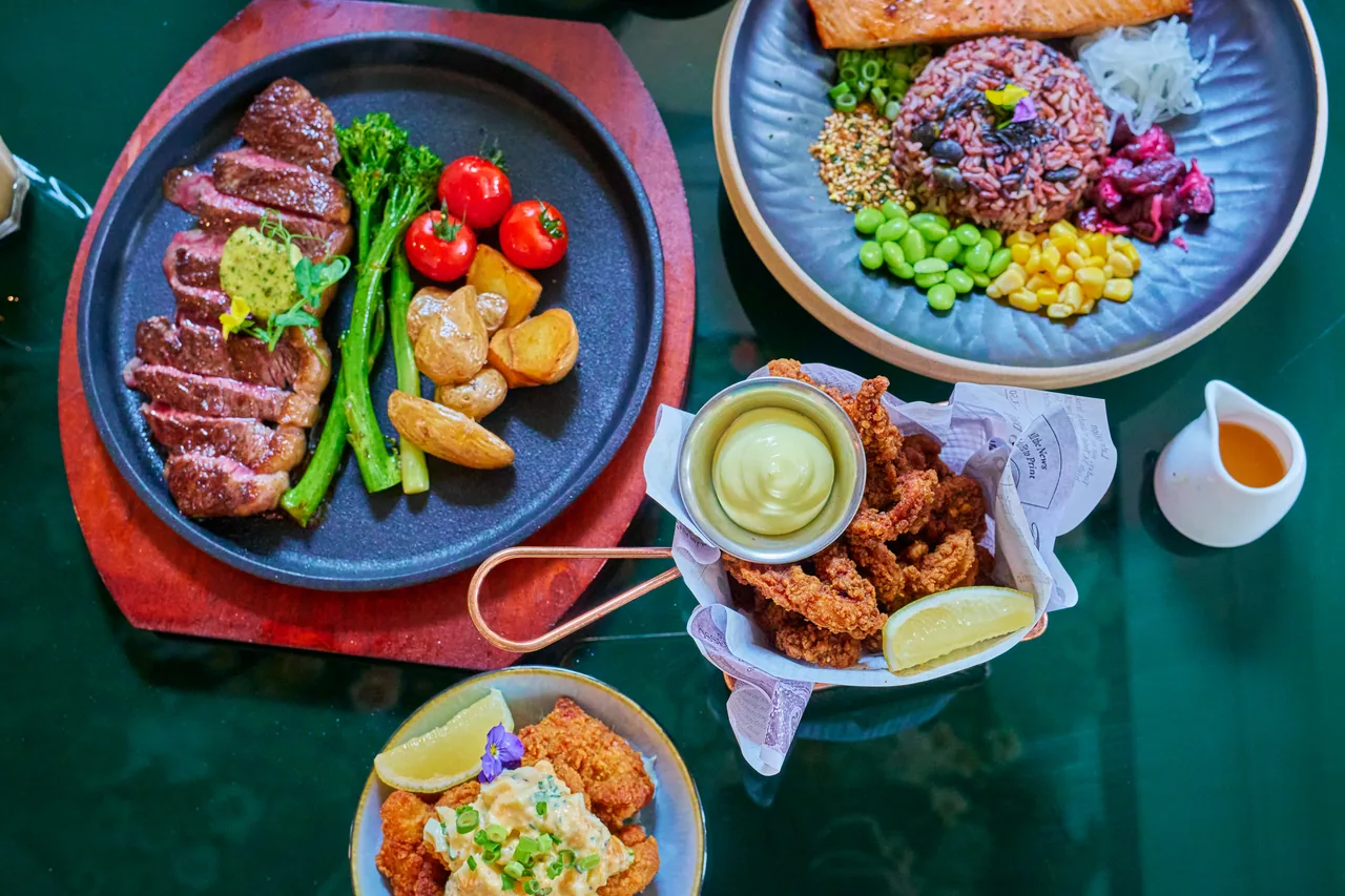 Overhead table spread of steak, a salmon rice bowl and fried chicken