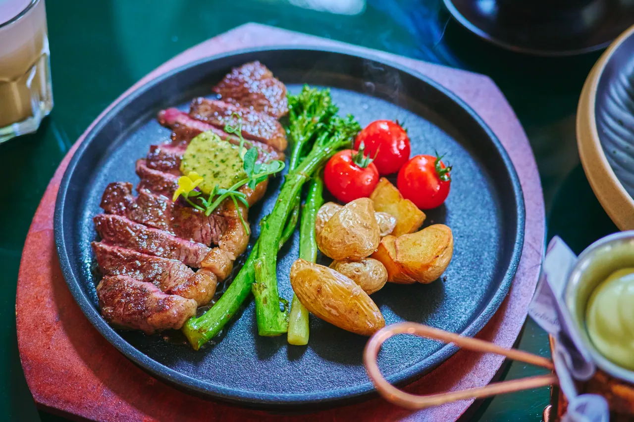 Sliced steak on a hot plate with broccolini, cherry tomatoes and roast potatoes
