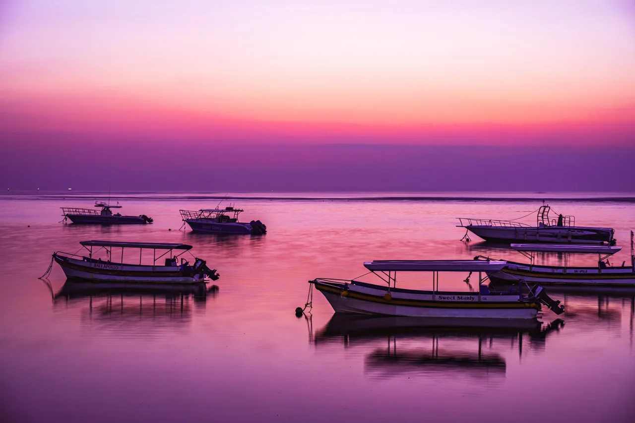 Small boats resting on still water under a pink and purple dawn sky