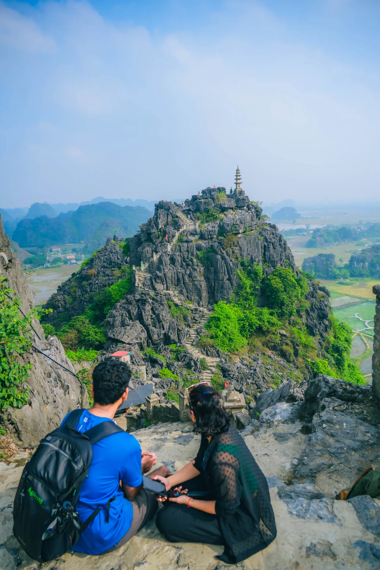Two hikers resting on a limestone peak with a small pagoda at the top