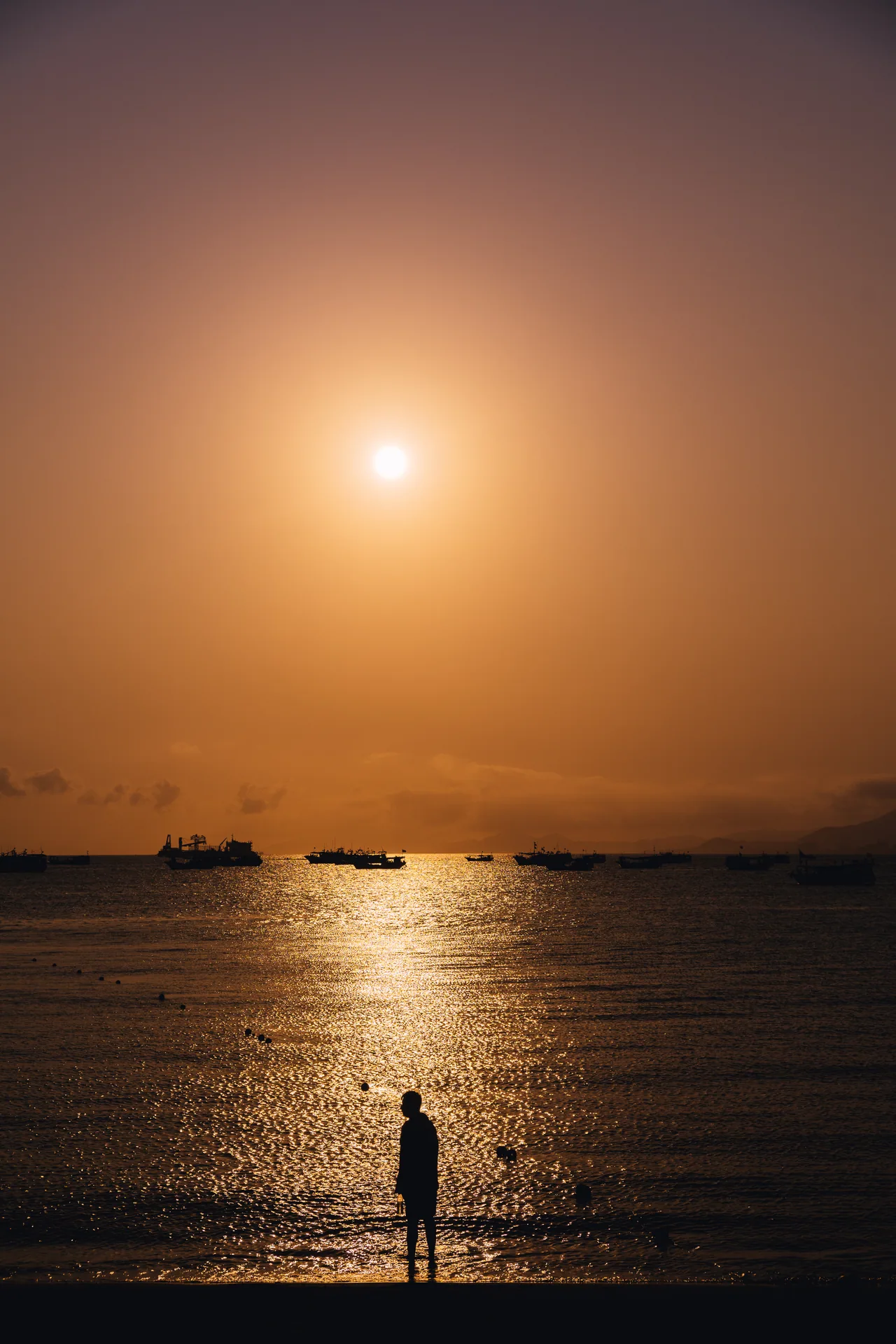 Sun setting over the sea with a lone figure silhouetted on the shore