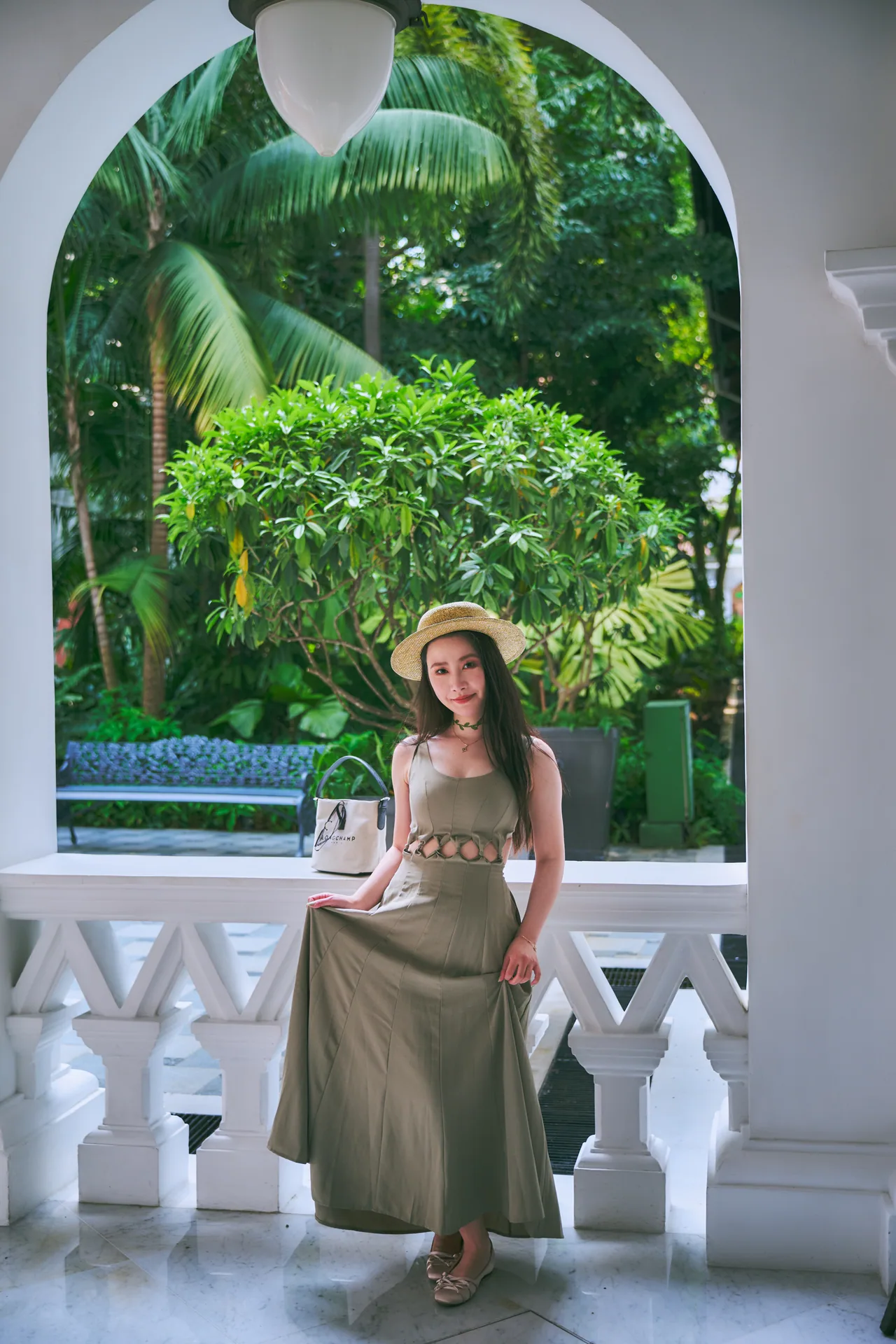 Woman in a long dress framed by a white arch and palm trees at Raffles Hotel