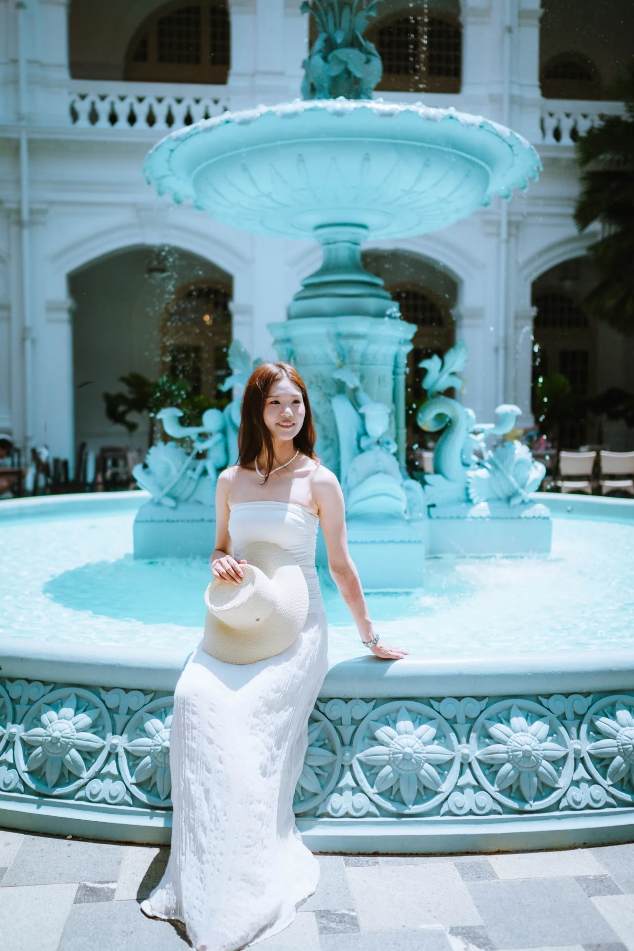 Woman in a white dress beside the fountain in a Raffles Hotel courtyard