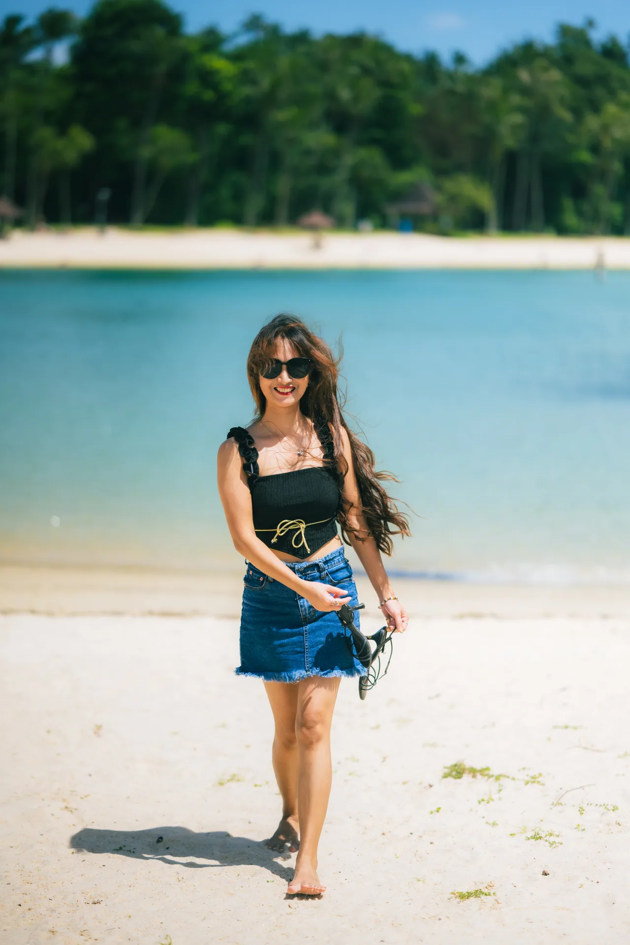 Woman walking on a white sand beach with the sea behind
