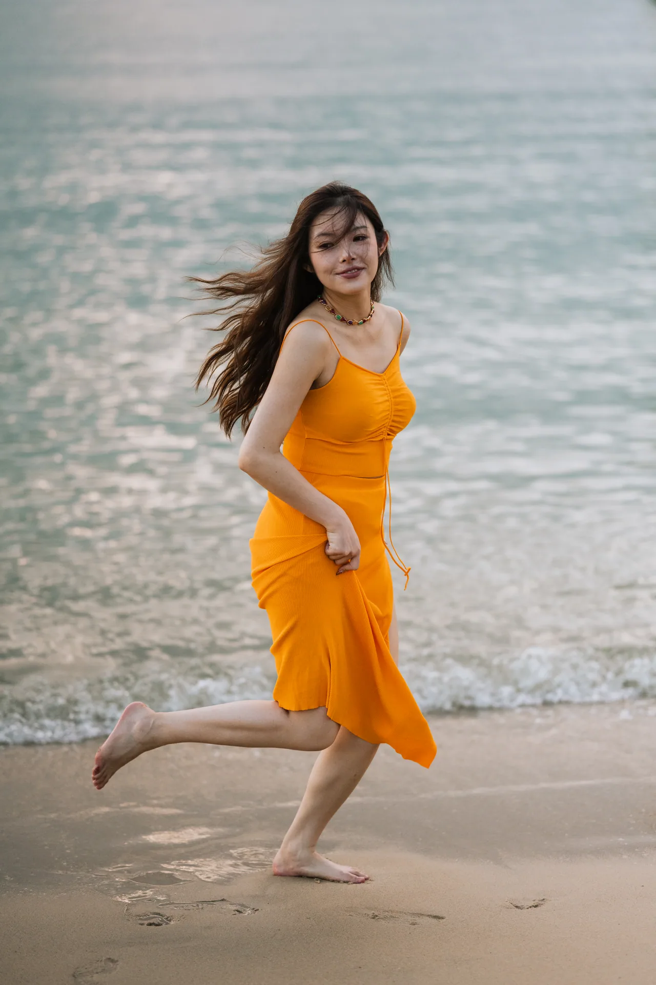 Woman in an orange dress running along the beach