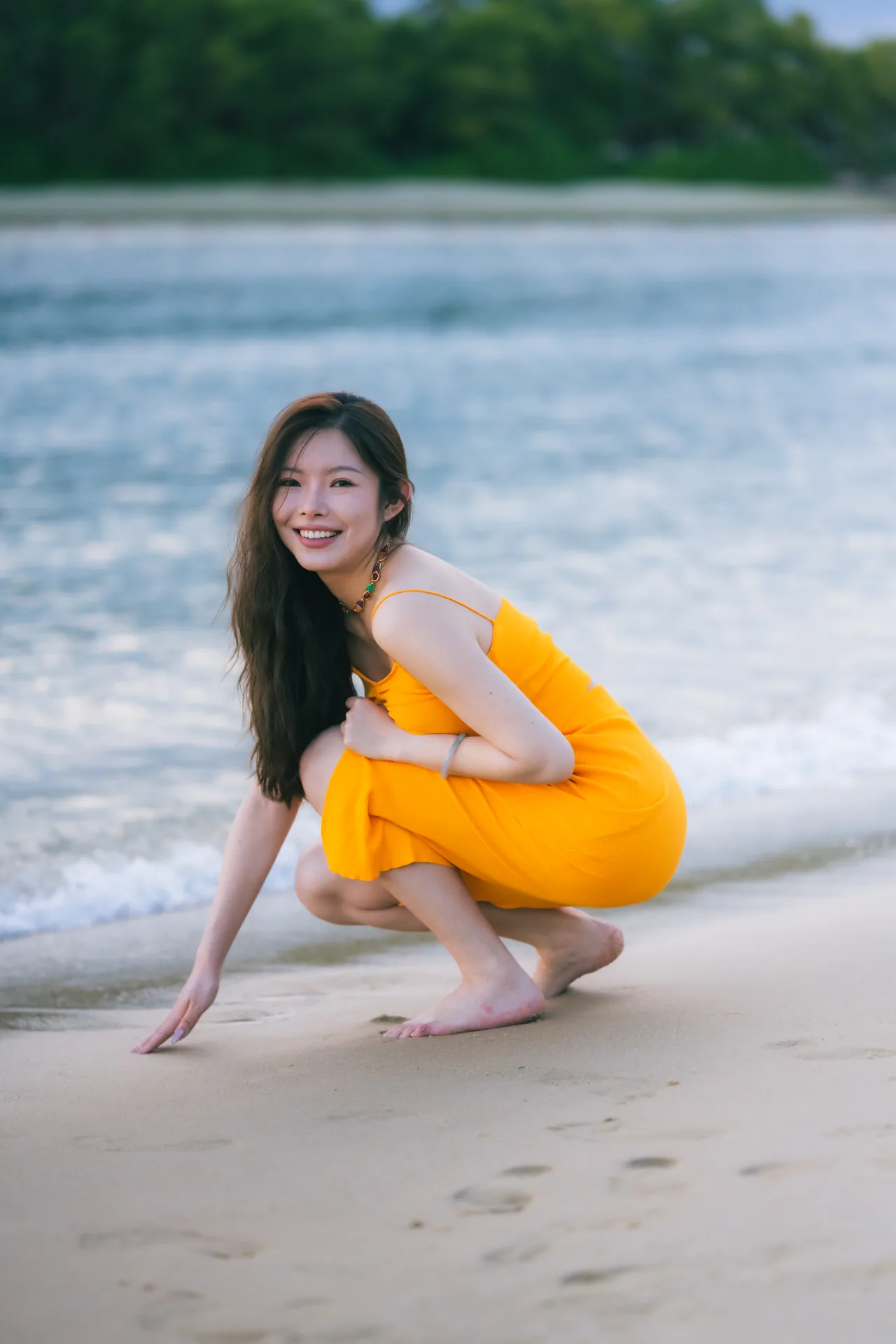 Woman in an orange dress crouching on the sand by the sea